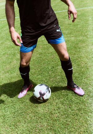 Black athletic shirt, blue-accented shorts, pink and black patterned soccer cleats. A black and white soccer ball on grassy field.