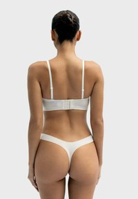 White lingerie set featuring a seamless underwire bra with adjustable straps and a thong with minimal coverage. Smooth fabric texture.
