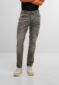 Jeans grii, uzate, cu croială dreaptă, având găuri și stropi de vopsea albastră. Include un accent roșu pe talie.
