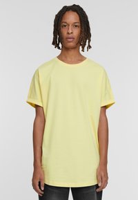 Camiseta amarilla de gran tamaño, fabricada en algodón suave, con cuello redondo, mangas cortas y un corte holgado. Sin patrones visibles ni elementos metálicos.
