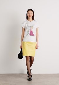 White cotton t-shirt with a colorful graphic print, paired with a yellow pencil skirt, black handbag, and dark stockings.