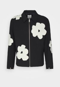 Chaqueta negra con cierre de cremallera, que presenta grandes apliques de flores blancas. Tiene un collar clásico y botones de presión en los puños.
