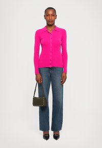Pink ribbed long-sleeve cardigan with a collar and buttons, paired with wide-leg blue jeans and a small olive green purse. Black pointed heels.
