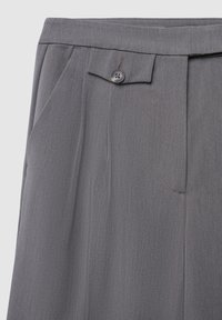 Pantaloni grigi con pieghe, dotati di chiusura con un solo bottone, tasche laterali e una texture liscia. Il tessuto presenta sottili linee verticali.
