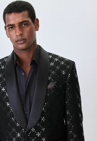 Fekete flitteres bl�ézer selymes hajtókával, mintás textúrával és szürke zsebkendővel. Sötét mintás ing felett viselve.