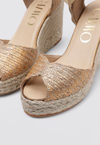 Sandalias de plataforma tejidas en dorado con diseño de punta descubierta, que cuentan con una cuña de yute trenzado y un forro interior suave.