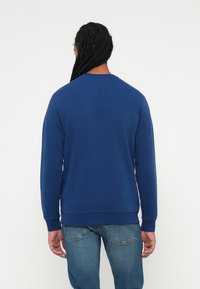 Sudadera azul marino con cuello redondo, mangas largas, puños y dobladillo acanalados. Tejido suave, corte recto. Combinada con jeans azul claro.