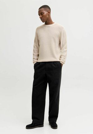 Suéter beige texturizado de manga larga, combinado con pantalones negros holgados y zapatos negros, creando una paleta de colores neutros.