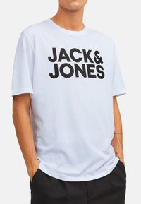 White cotton t-shirt featuring bold black text "JACK & JONES." Short sleeves, round neckline, relaxed fit. Smooth texture, casual design.