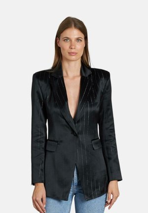Blazer de satén negro con rayas, solapas con muescas, dos bolsillos delanteros y escote en V profundo, ajuste entallado. Combinado con jeans azules.