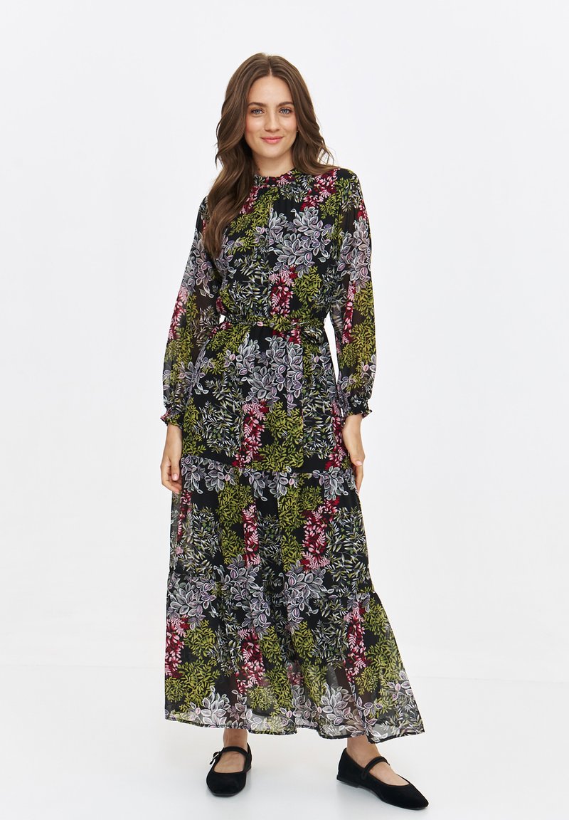 Long, sheer black dress with a floral pattern in green, pink, and white. Elastic waist, long sleeves, and tiered skirt. Worn with black flats.