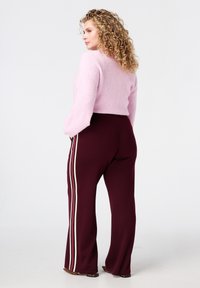 Lichtroze cropped sweater met een zachte textuur, gecombineerd met kastanjebruine broeken met witte zijstrepen. De sweater heeft losse mouwen.