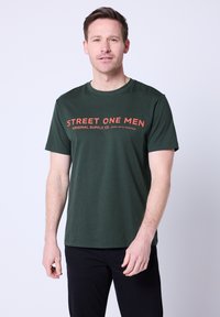 Ciemnozielona bawełniana koszulka z okrągłym dekoltem i krótkimi rękawami, z czerwonym napisem "STREET ONE MEN" na piersi.