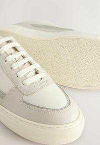 Weiße Leder-Sneaker mit glatter Oberfläche, runder Zehenpartie und strukturiertem Schuhsohle. Merkmale sind tonales Nähen und flache Schnürsenkel. Texturierte Außensohle mit Branding.