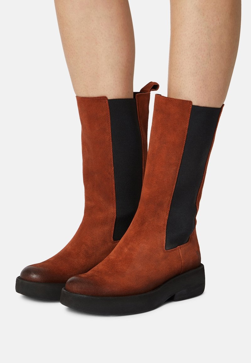 Brązowe zamszowe botki za kostkę z czarnymi elastycznymi panelami bocznymi i zaokrąglonym noskiem, wyposażone w grubą czarną podeszwę dla dodatkowego komfortu.