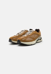 Brune suede sneakers med mesh-detaljer, hvide snørebånd og en kraftig sort gummisål. Har et fremtrædende brandlogo på siden.