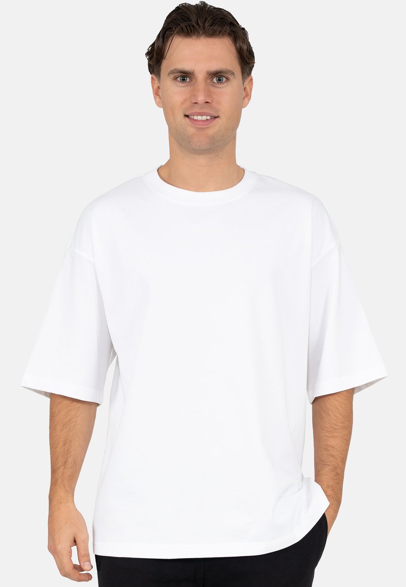 Witte T-shirt met korte mouwen, een ronde hals, een losse pasvorm, een gladde textuur en minimale naden, gedragen door een persoon.