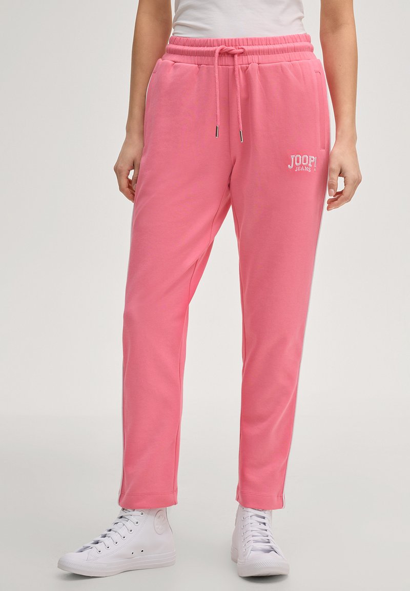 Persona che indossa pantaloni della tuta rosa con coulisse e logo "JOOP! JEANS" sulla coscia, abbinati a sneakers bianche alte.