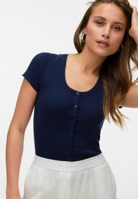 Jūras spēku zila ribota adīta T-kreklu ar īsām piedurknēm un apaļu izgriezumu, priekšā ar sešiem pogu aizdari, kombinēta ar gaišiem apakšveļas gabaliem.