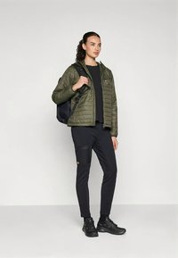 Zaļa dūnu jaka ar rāvējslēdzēju, melns tops un bikses, melna mugursoma un melni apavi. Ievērojama kabata uz biksēm. Ikdienišķs stils.