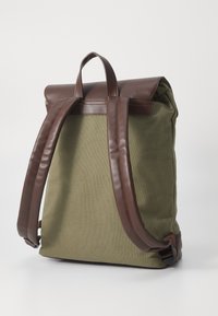 Zaino in tela verde oliva con patta e spallacci in pelle marrone, dotato di manico superiore e di una forma rettangolare elegante.