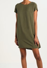 Robe verte olive à manches courtes avec col rond, coupe décontractée, fentes latérales et texture douce. Tissu léger, longueur genou.