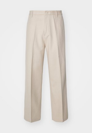 Pantalones beiges a medida con un corte recto, que destacan por su textura suave, línea de pliegue central y cinturilla estándar con presillas para el cinturón.