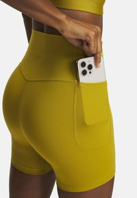 Geel hoge sportshorts met een zijzak waarin een smartphone zich bevindt. Gemaakt van een rekbare, gladde stof met zichtbare stiksels.