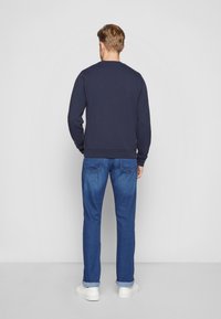 Sweatshirt in cotone navy con maniche lunghe, scollo a girocollo e polsini a costine, abbinato a jeans in denim blu e sneakers bianche.