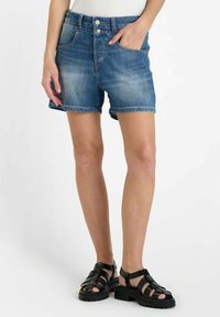 Leren denim short in lichtblauw met een iets vervaagde afwerking, opgerolde zoom, vijf zakken en een rits, gecombineerd met zwarte sandalen met bandjes.