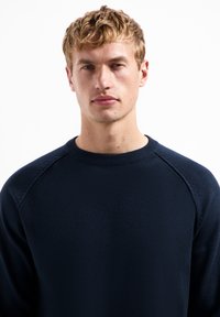 Marineblauwe gebreide trui met geribbelde textuur, ronde halslijn en raglanmouwen. Eenvoudig ontwerp zonder patronen of zichtbare hardware.