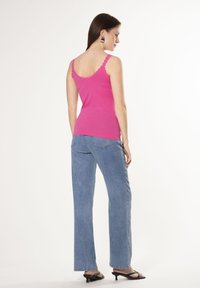 Top de tirantes rosa ajustado con bordes en forma de concha, combinado con unos jeans de pierna ancha de color azul claro. Modelo llevando sandalias negras con tacón, visto desde atrás.