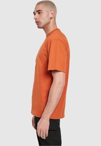 Korte mouwen t-shirt in verbrand oranje katoen. Rechte snit, ronde halslijn, met een zachte textuur. Draag met zwarte cargo-broeken, voor een neutrale achtergrond.