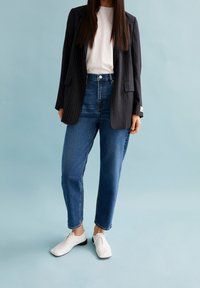 Černý sako s pruhy, bílé tričko, džíny s vysokým pasem v modré barvě a bílé boty s kulatou špičkou. Jednoduchý a čistý design, minimální akcenty.