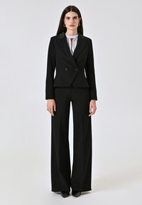 Completo elegante nero composto da una giacca doppiopetto con grandi bottoni, abbinata a pantaloni a gamba larga. Tessuto liscio, design minimalista.