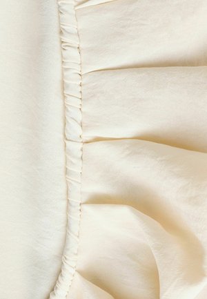 Helles beiges Gewebe mit einer gerafften Naht und feiner Stichführung, das eine glatte Textur und einen subtilen Glanz zeigt.