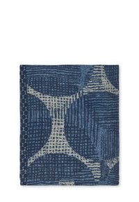 Folde blå stof med abstrakte geometriske mønstre i lysere beige nuancer og teksturerede marineblå prikker langs en kant.