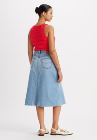 Top court tricoté rouge avec un motif ajouré, associé à une jupe en denim bleu clair de mi-longueur, avec un ourlet brut et des poches arrière.