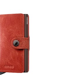 Monedero de cuero en naranja quemado con cierre de botón a presión, que cuenta con un elegante soporte metálico para tarjetas y una marca grabada.