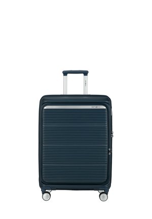 Dark blue hard-shell suitcase with horizontal ridges, telescopic handle, and four swivel wheels, standing upright on a white background.