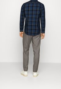 Granatowa koszula w kratę z długimi rękawami, detalami zapinanymi na guziki przy mankietach oraz zaokrąglonym dołem, w połączeniu z jasnoszarymi, dopasowanymi spodniami i białymi trampkami.