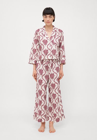 Kjolepyjamas med hvit bunn og burgunder blomsterdesign. Har en krage topp og bred-bein bukser. Myk tekstur, avslappet passform.