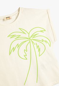 Camiseta de algodón color crema con un diseño de palmera en neón verde, con costuras detalladas que recuerdan a las hojas y el tronco. Mangas cortas, escote redondeado.
