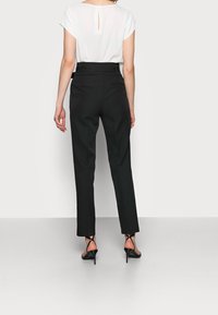 Zwarte op maat gemaakte broek met een rechte pijp, gecombineerd met een witte top met een uitsparing op de rug. Het model staat op zwarte hakken.