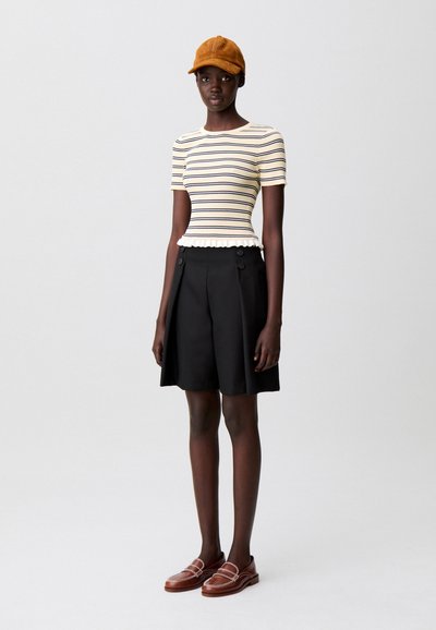 Top de canalé a rayas en crema y azul marino, pantalones cortos plisados negros con botones, mocasines marrones y una gorra marrón. Diseño simple y clásico.