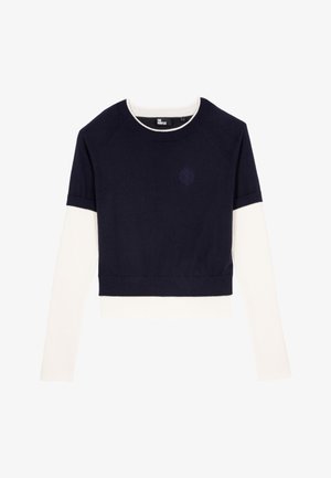 Marineblauwe en crème cropped trui met lange witte mouwen, ribbelkraag en zoom, voorzien van geborduurd logo op de borst, zachte textuur.