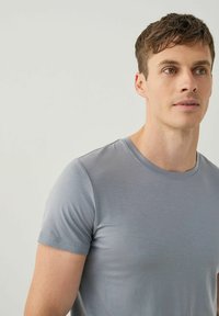 Vaaleanharmaa lyhythihainen t-paita, joka on valmistettu sileästä kankaasta, klassisella pyöreällä pääntiellä ja vartalonmyötäisellä muotoilulla, jossa on hienovarainen rakenne.