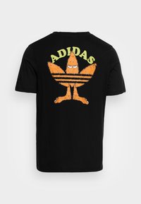 Maglietta nera con un logo Adidas in peluche arancione stilizzato che assomiglia a un uccello imbronciato e la scritta "ADIDAS" sopra di esso sul retro.