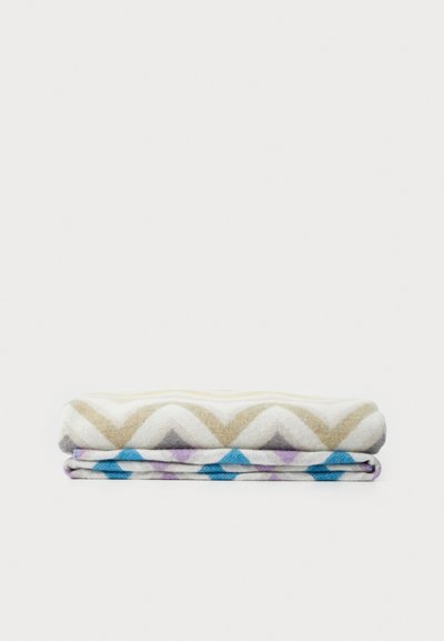 Two folded blankets, one with a beige zigzag pattern on a light background, and the other with blue and purple diamond shapes on white.