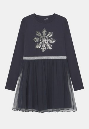 Robe longue à manches longues pour filles en bleu marine avec un flocon de neige en sequins argentés sur la poitrine, une ceinture argentée et une superposition de jupe en tulle.